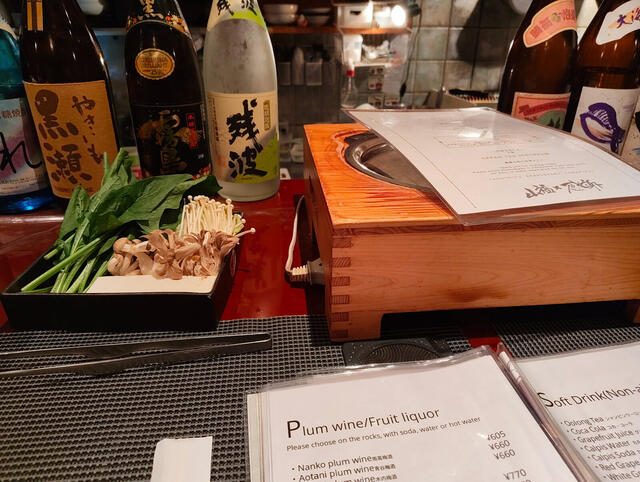 Sukiyaki en la barra: carne finisima rosada en bandeja de madera (parece cerdo, quiza agu de Okinawa), verduras y olla de bronce sobre base de madera. Cerveza Kirin Master's Dream, highball y botellas de awamori Zanpa detras del mostrador.