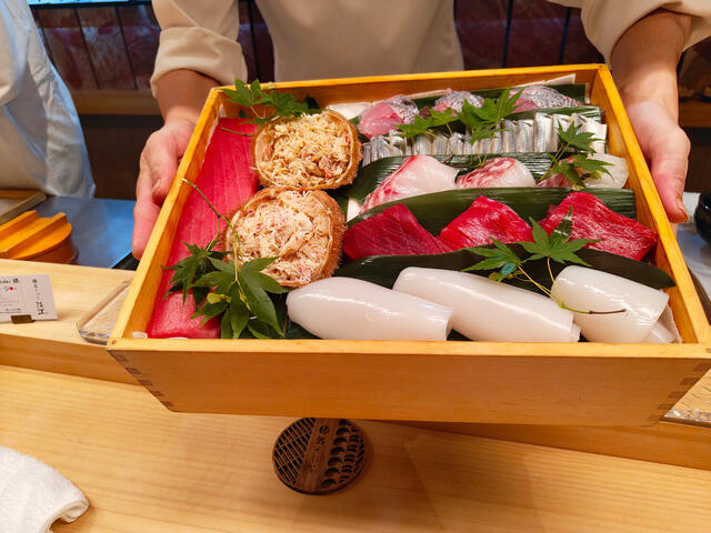 Omakase de sushi en barra: la caja de atún, el pescado sobre hojas y una cerveza.