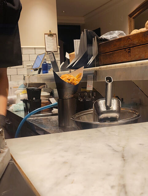 Cono de papas fritas belgas con salsa naranja (tipo andalouse) y bebida amarilla en vaso con logo "Frites", compradas para llevar y comidas por Gion bajo la lluvia.
