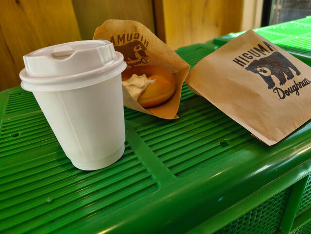 Un doughnut relleno de crema y un cafe caliente en vaso para llevar, comidos en la calle.